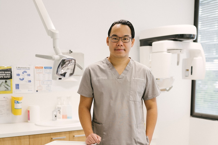 A man in scrubs with glasses in front of dental machines