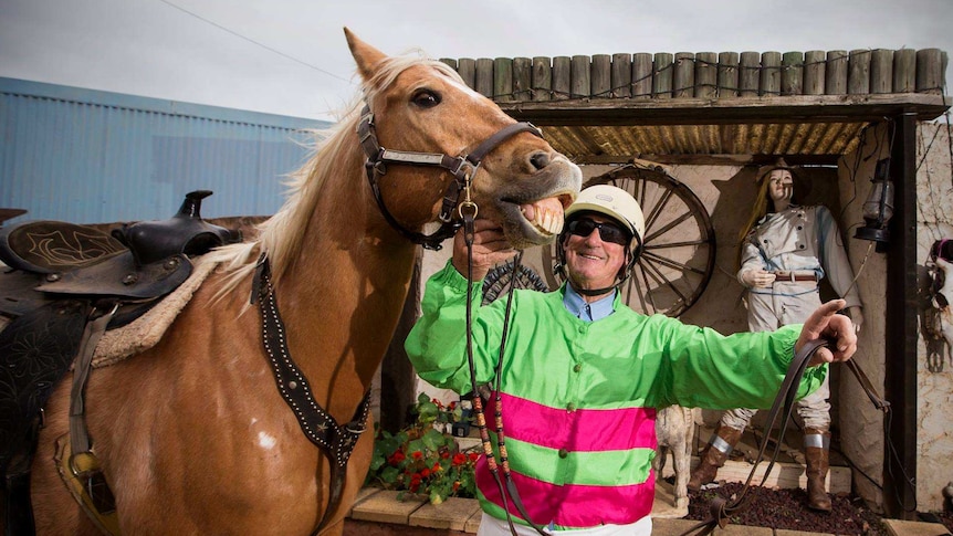 A man in harness racing gear next to a golden horse