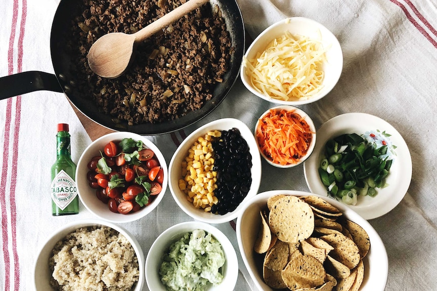 Frying pan with spiced mince meat and various bowls containing taco bowl ingredients