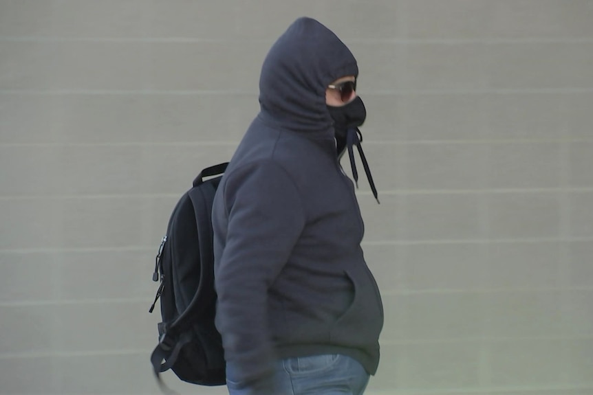 A man wearing a black hoodie tied around his face and sunglasses.