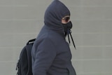 A man wearing a black hoodie tied around his face and sunglasses.