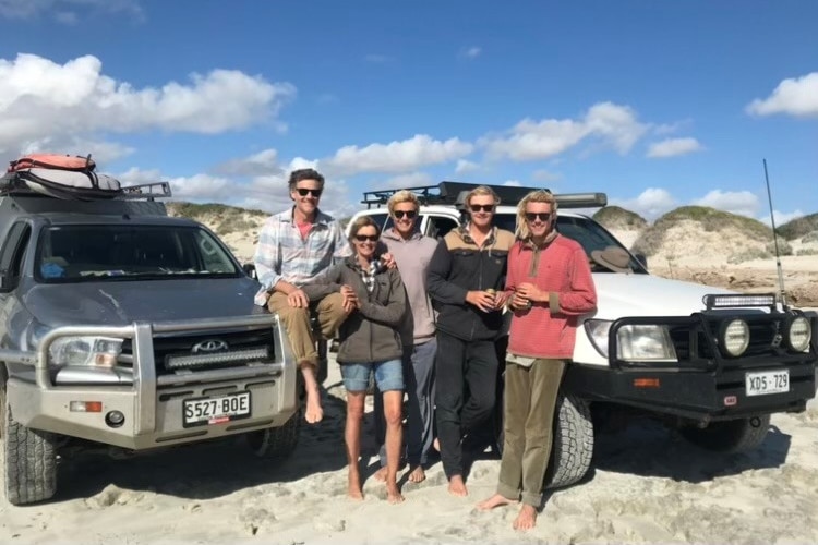 A family stands next to their 4WD vehicle in a sandy area, including a man and woman and their three adult children.