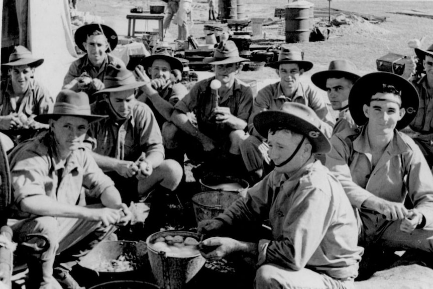 A black and white photograph showing a group of young soldiers sitting on the ground peeling potatoes.