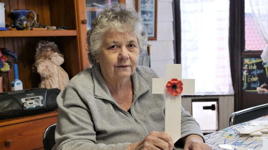 A woman holds a small white cross with a poppy attached to it