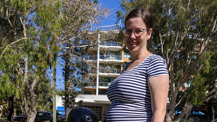 A pregnant woman smiles as she stands with her young son in the playground.