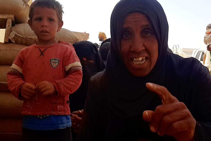 A woman points her finger at the lens as a young boy stands next to her.