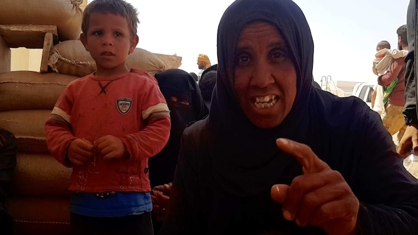 A woman points her finger at the lens as a young boy stands next to her.