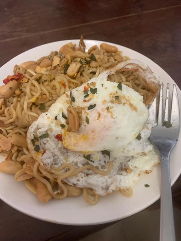 A plate of noodles with a fried egg and anchovy, peanut and chilli on top.