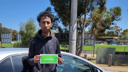 A young man stands in a car park on a sunny day.