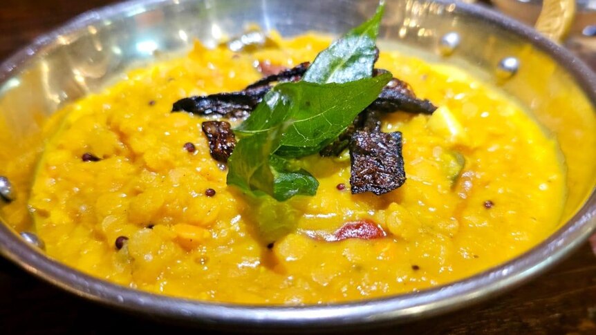 A bowl of lentil curry yellow in colour in a silver metal dish