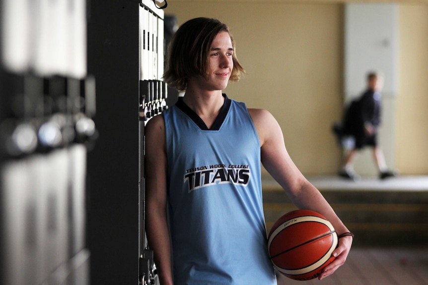 Teenager leaning against school lockers with a basketball