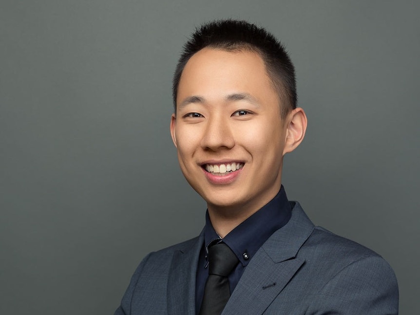 Thomas Tang smiles with his arms crossed wearing a dark grey blazer.