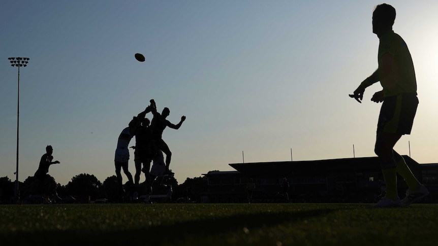 A silhouette of a ruck contest in an Australian rules match.