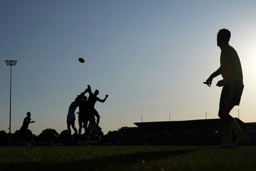 A silhouette of a ruck contest in an Australian rules match.