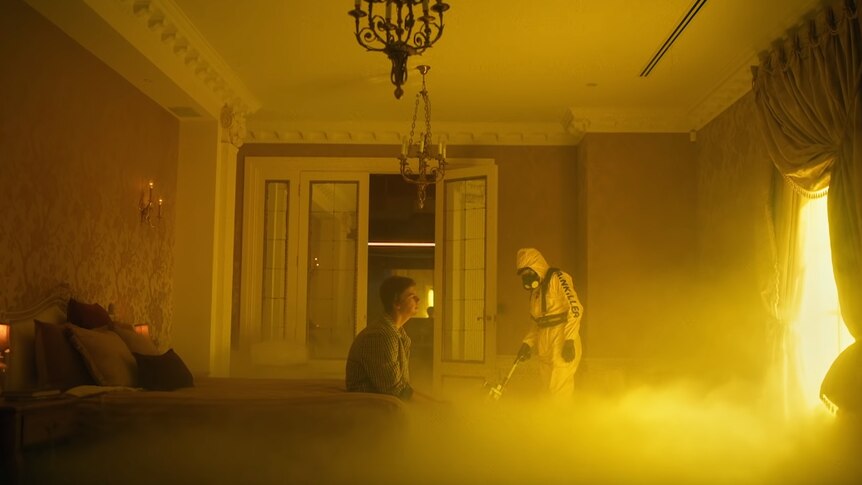 Still from Ruel's Painkiller music video, sitting on a bed with exterminator in the background
