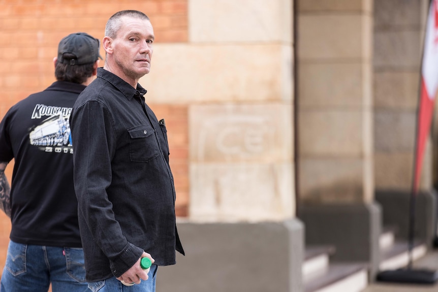 A man in a black shirt waiting outside court.  