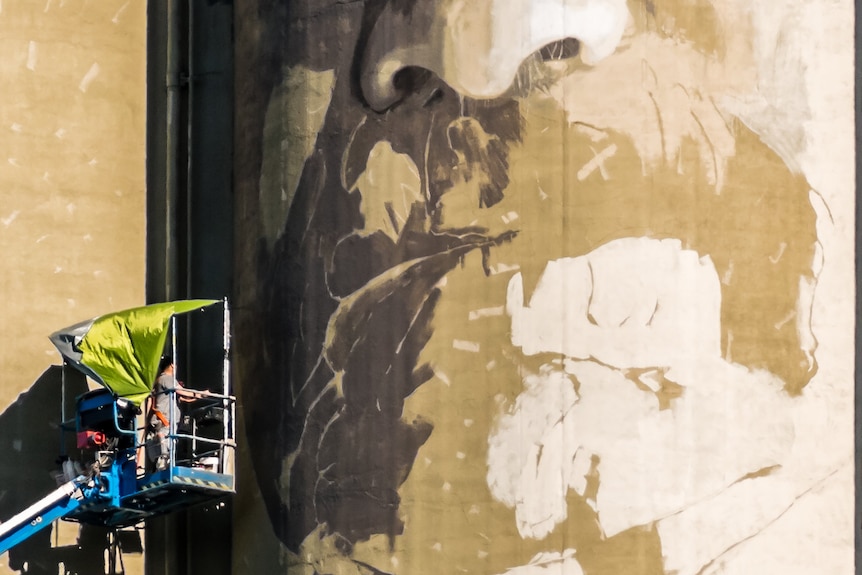 A man on a boom lift paints a huge portrait