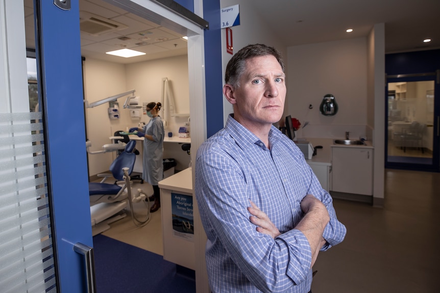 A man with his arms folded standing in front of a dental room.