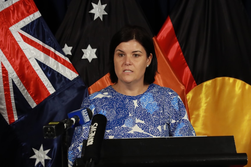 a woman with short dark hair speaking at a lecturn in front of australian flag