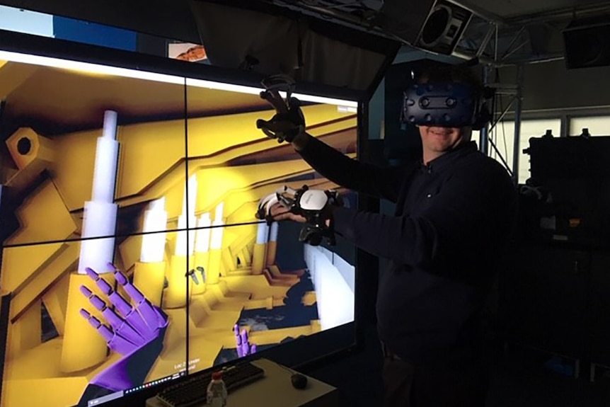 Scientist Peter Reid stands in front of virtual reality screen and using VR technology helmet and hands.