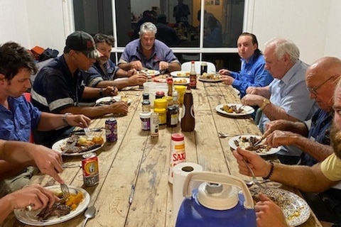 Workers are seated around a long table eating dinner.