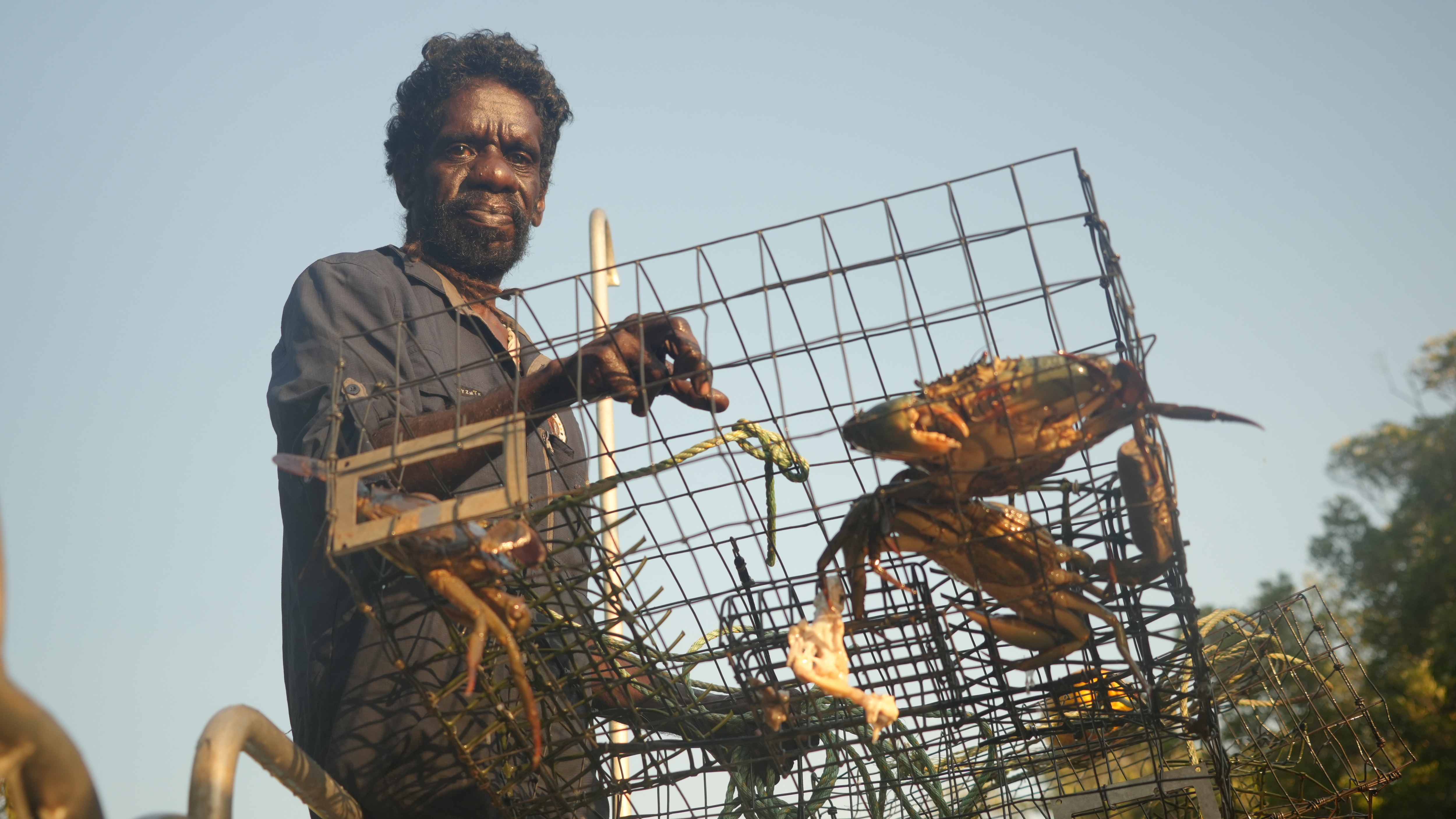 An Indigenous man holding a cage with mud crabs inside.