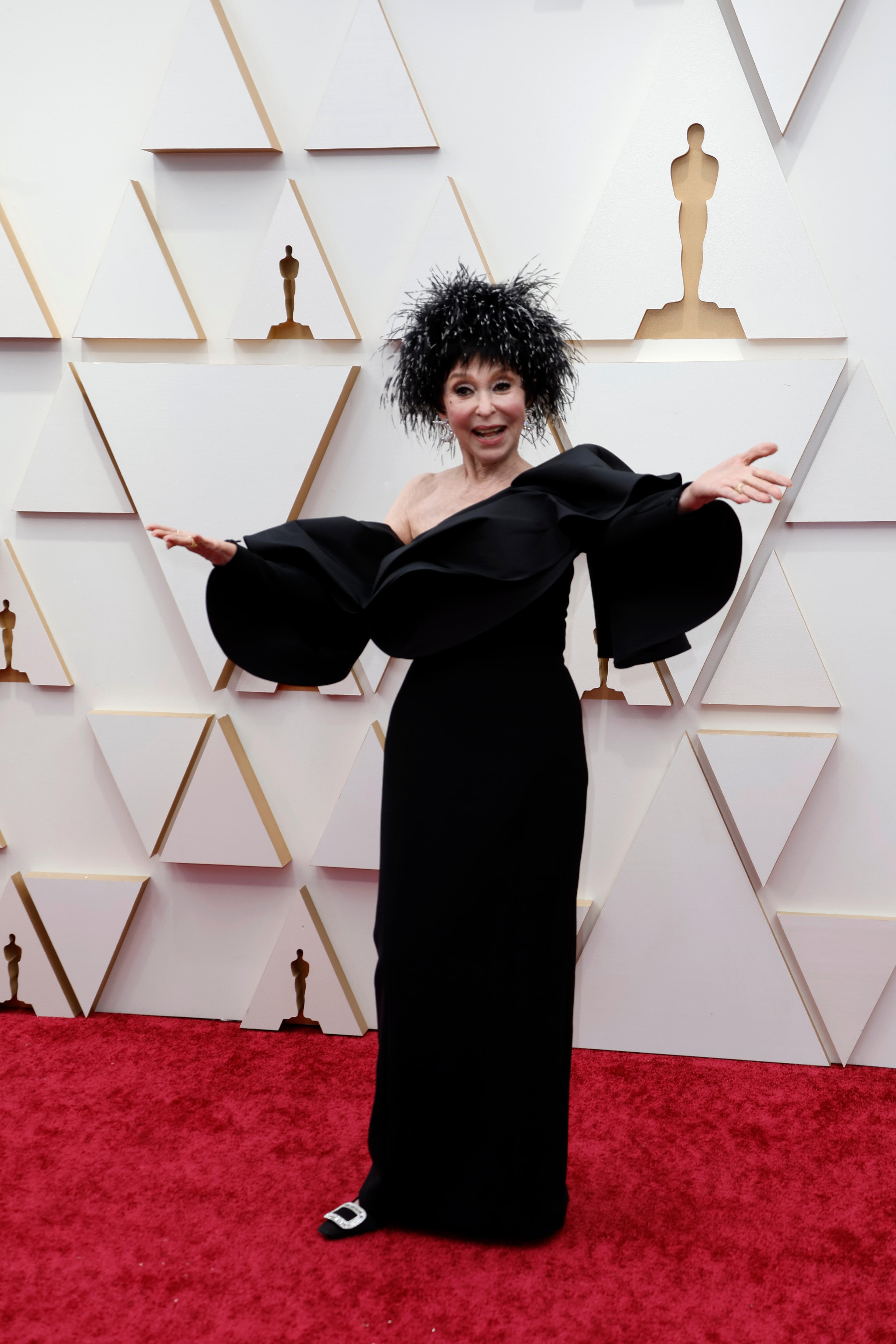 Rita Moreno wearing long black off-the-shoulder gown with a fluffy black metallic hat