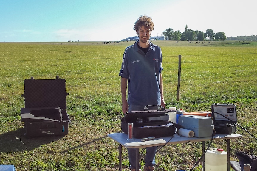 A man stands in a paddock in front of a table with lots of boxes and screens on it.