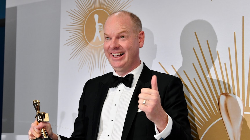 Tom Gleeson stands holding a small logie statue i