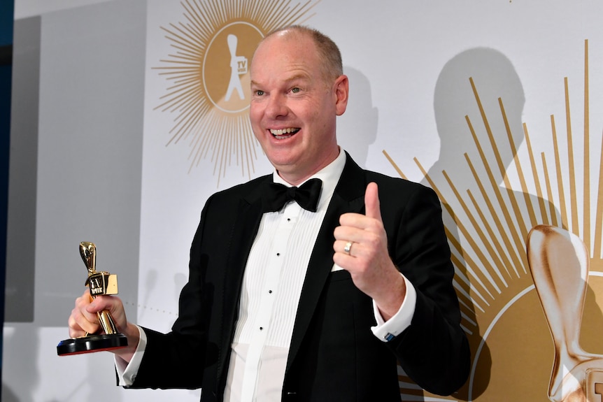 Tom Gleeson stands holding a small logie statue i