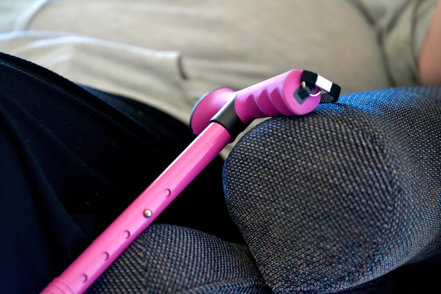 A pink walking stick leaning up against an arm chair. 