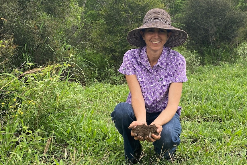 A woman wearing a hat holds a handful of dirt