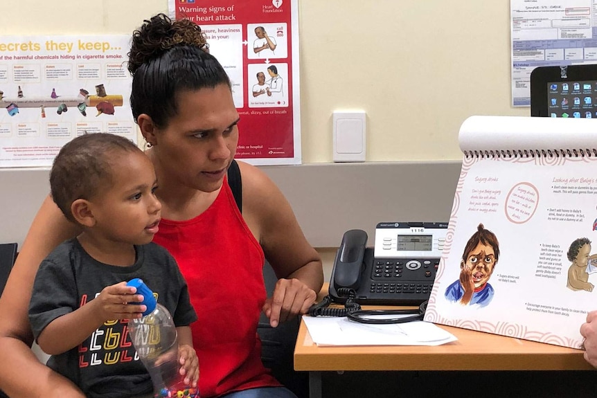 Siegrid David and her two-year-old son Zekaniah Bon sit at a desk in a health clinic.