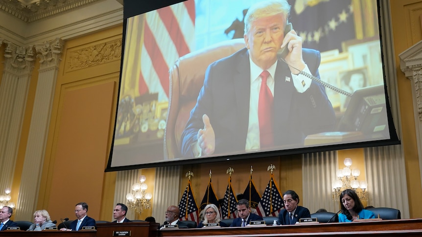 An image of Donald Trump talking on a telephone appears on a projector screen above a number of officials sitting at a long desk
