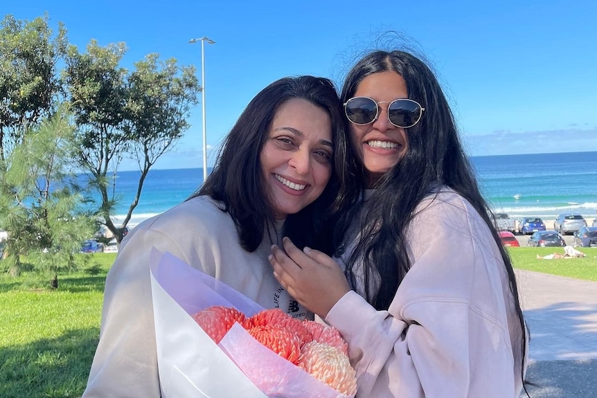 Two women smile while posing next to each other for a photo on the beach.