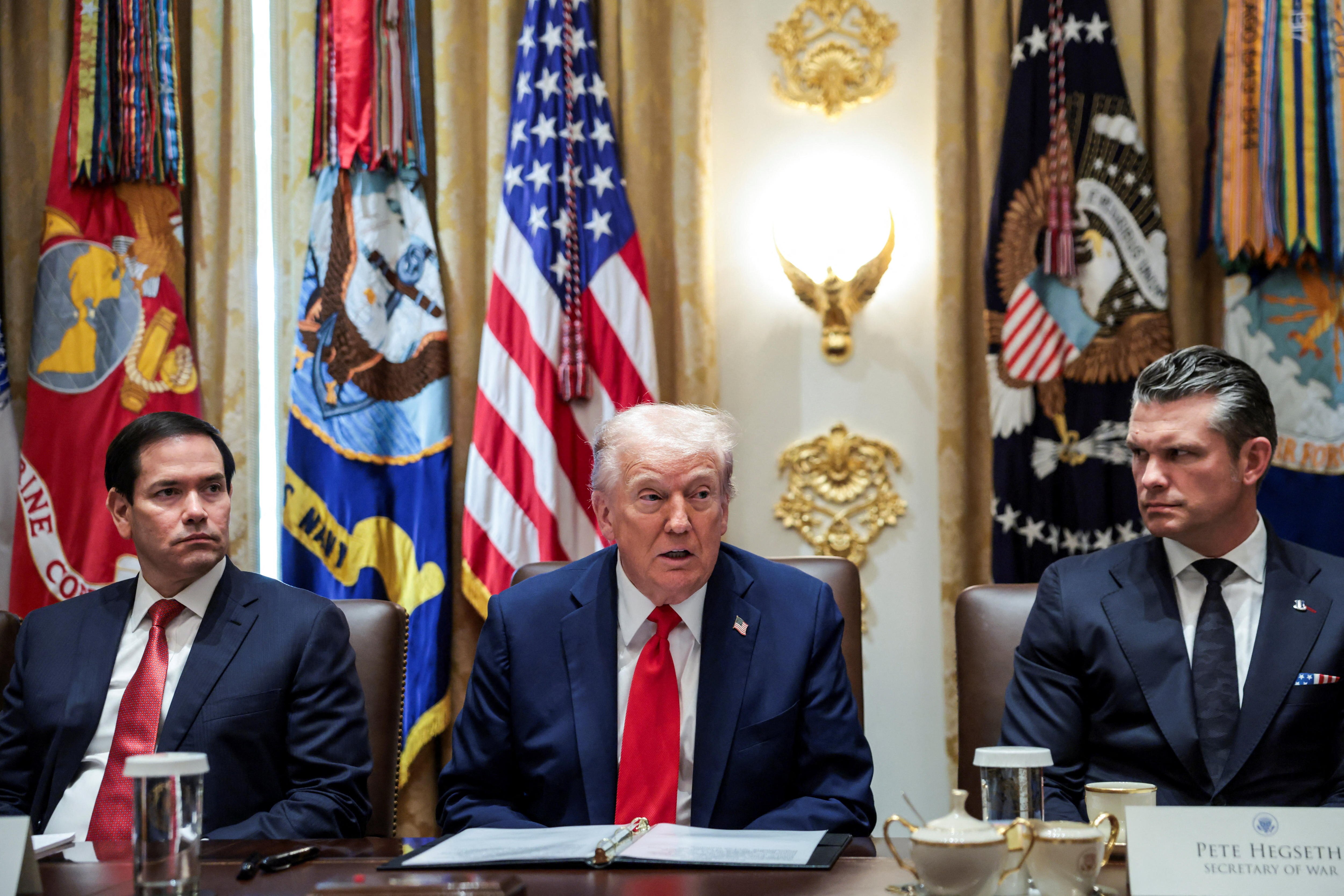 Donald trump sitting at a desk with flags behind him