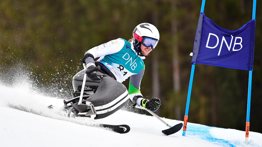 Man in a seated ski going past a gate 