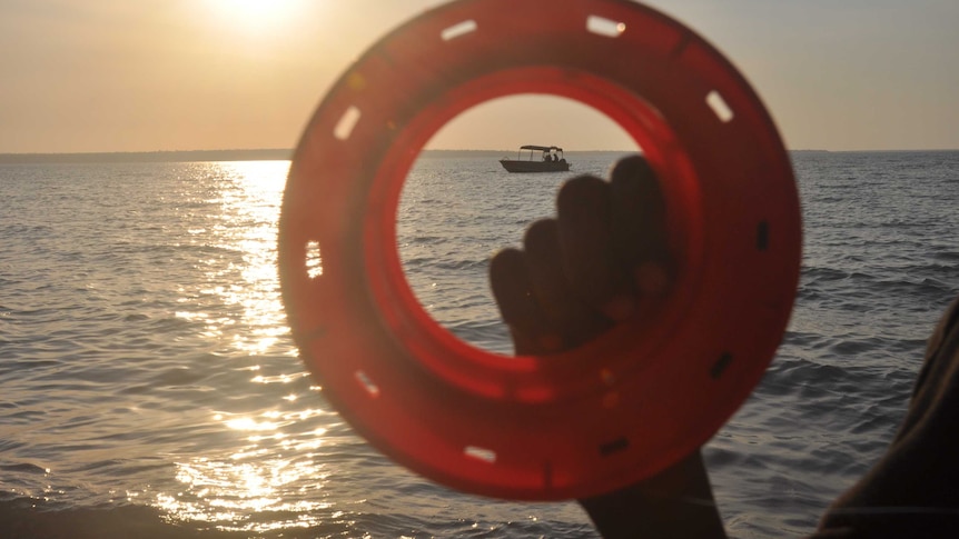 A fishing reel held up to the sun by a young Aboriginal person's hand.