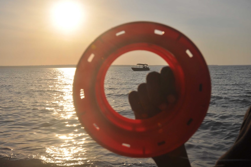 A fishing reel held up to the sun by a young Aboriginal person's hand.