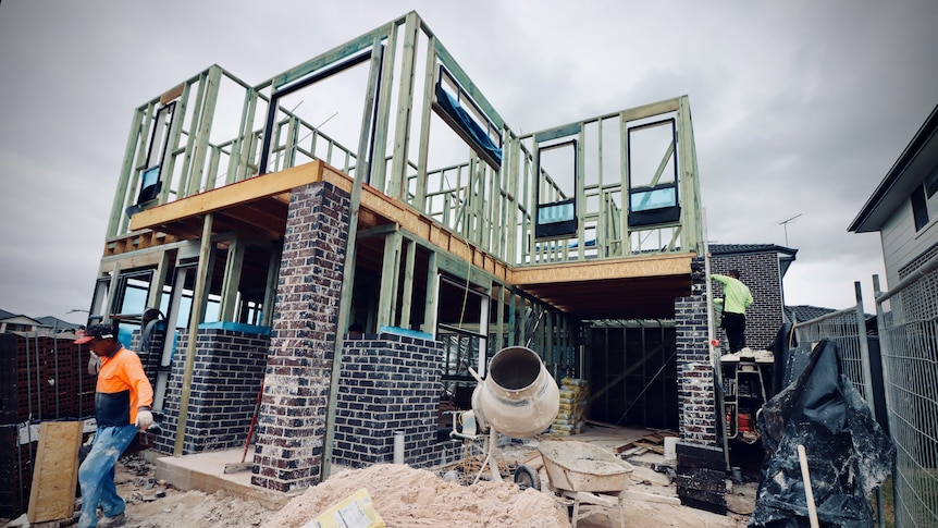 Two men are building a house. A cement mixer sits in the foreground of the construction site.