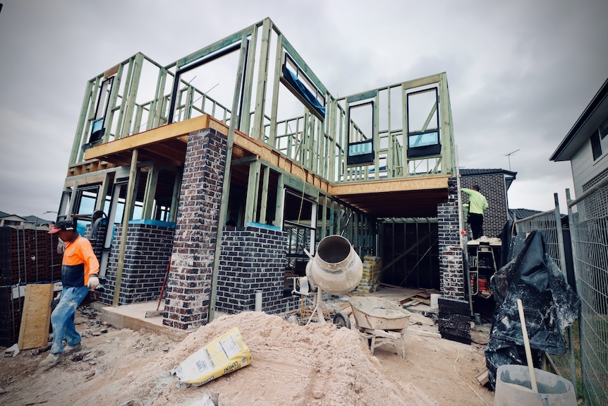 Two men are building a house. A cement mixer sits in the foreground of the construction site.