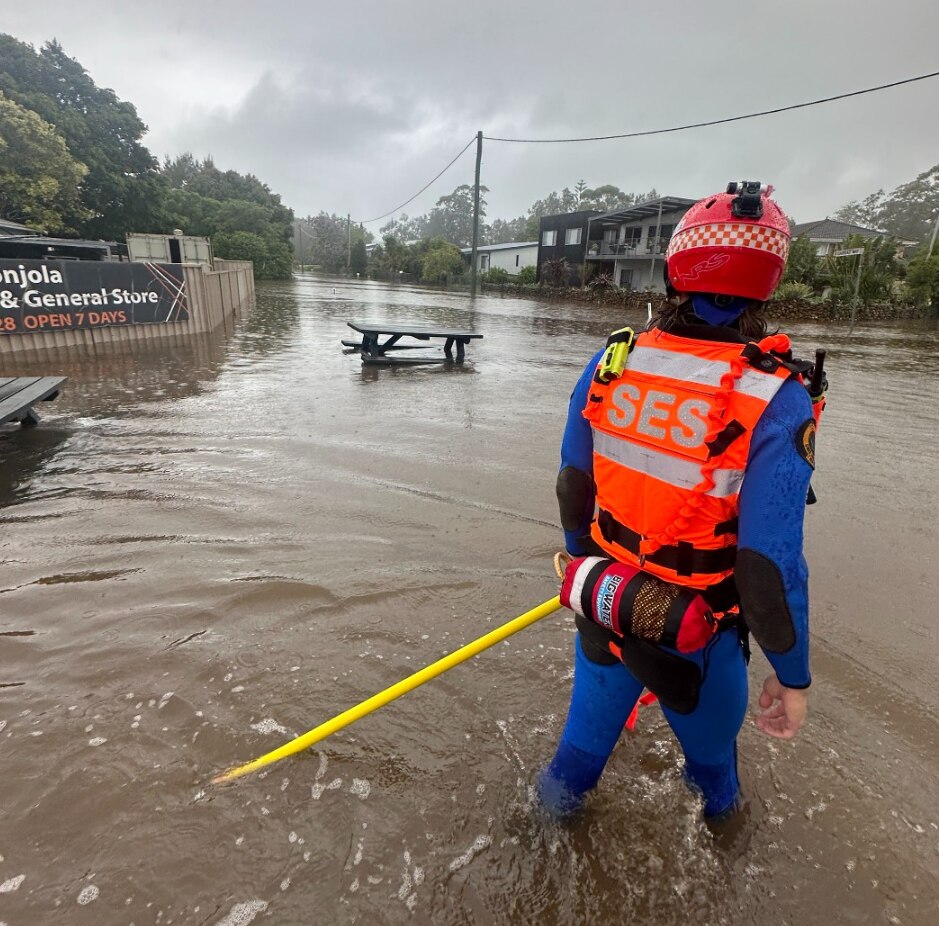 A person in high-vis with SES branding looks down a flooded street in a regional town.
