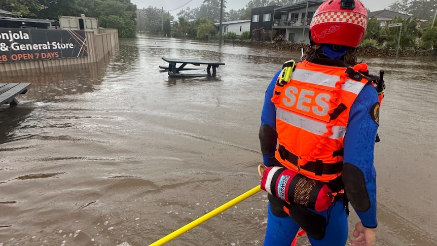 A person in high-vis with SES branding looks down a flooded street in a regional town.