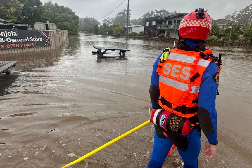 A person in high-vis with SES branding looks down a flooded street in a regional town.