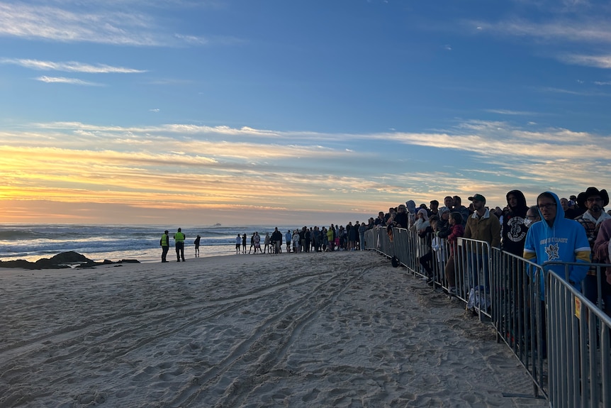 Eine große Menschenmenge hinter einem Zaun am Strand im Morgengrauen