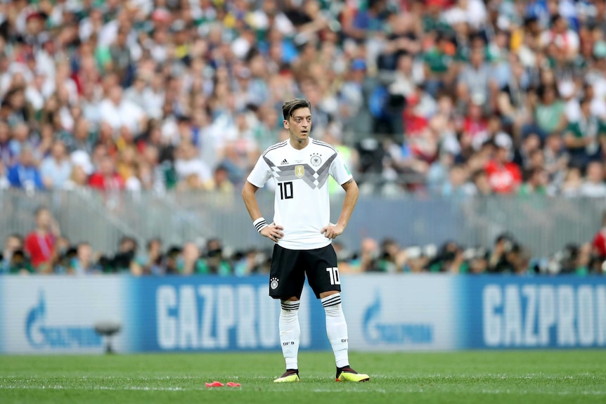 Mesut Ozil stands on his own in the centre of the pitch with his hands on his sides.