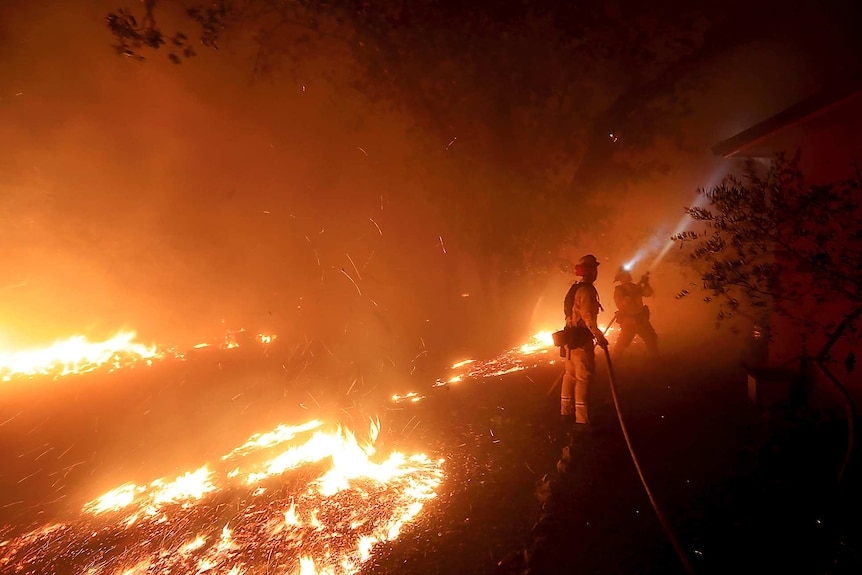 Two firemen use hoses to battle intense wildfires.