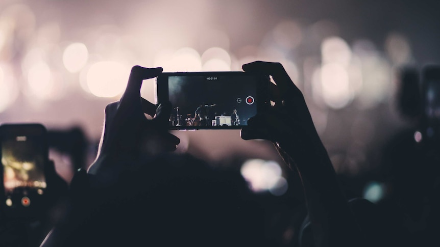 Hands hold up a phone at a gig