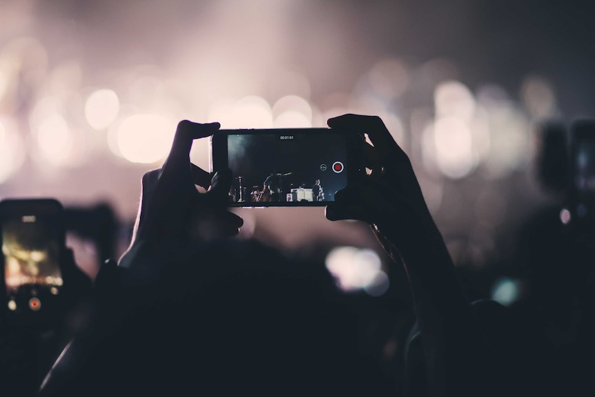 Hands hold up a phone at a gig