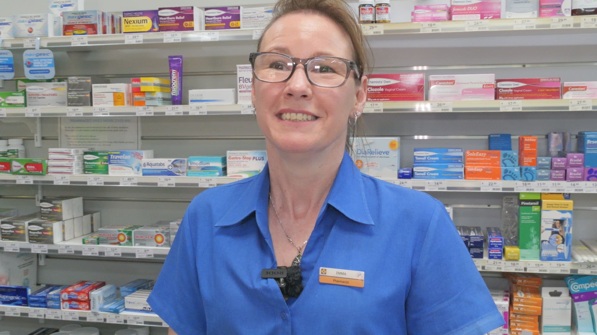 Una mujer está detrás del mostrador de una farmacia, detrás de ella hay un botiquín